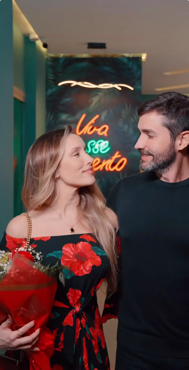 Casal se olhando em frente ao neon Viva esse momento no salão do Ykedin