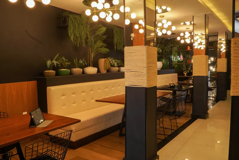 Salão do Ykedin com sofá capitonê, plantas, luminárias de globos e tablets nas mesas